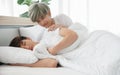 Young Asian attractive gay man smile and provoke his boyfriend by hand put on his arm while his lover sleeping on bed in the morni Royalty Free Stock Photo