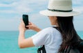 Young Asian backpacker woman wear hat use smartphone taking selfie at pier. Summer vacation at tropical paradise beach. Happy Royalty Free Stock Photo