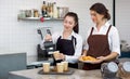 Young asian barista with a smile pouring milk from the jug into a paper coffee cup. Caucasian assistant in an apron holding Royalty Free Stock Photo