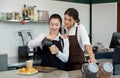 Young asian barista with a smile pouring milk from the jug into a paper coffee cup. Caucasian assistant in an apron stands