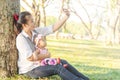 Young Asian beautiful mother using a smart phone selfie with her little girl 5 months daughter in park sunny day. Beautiful young Royalty Free Stock Photo