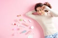 Young Asian beautiful woman smile with her cosmetic makeup tools - she is lying on the pink floor. Top view Royalty Free Stock Photo