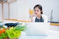 Young asian beautiful woman using a tablet for looking for recipe or learning cooking online with vegetables in kitchen at home, Royalty Free Stock Photo