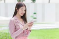 Young Asian beautiful working female in pink dress suit holds and looks at her smartphone happily in green natural background