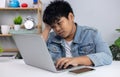 Young Asian boy in denim jacket looking bored and exhausted while using laptop, representing online learning fatigue, screen time Royalty Free Stock Photo