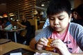 Young Asian boy eats a hamburger inside a fast food restaurant Royalty Free Stock Photo