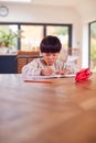 Young Asian Boy Home Schooling Working At Table In Kitchen Writing In Book Royalty Free Stock Photo