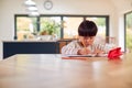 Young Asian Boy Home Schooling Working At Table In Kitchen Writing In Book Royalty Free Stock Photo