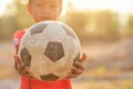 Young Asian boy playing old and dirty classic soccer ball in the morning