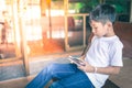 Young Asian boy sitting on a wooden chair playing mobile phones outside the house Royalty Free Stock Photo