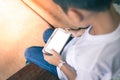 Young Asian boy sitting on a wooden chair playing mobile phones outside the house Royalty Free Stock Photo