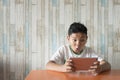 Young asian boy using digital tablet at the dining table at home with excited face.