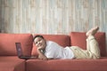 Young asian boy using laptop computer lying on a sofa at home while looking at camera. Royalty Free Stock Photo