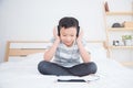 Young boy wearing headset listening music and play games from tablet computer on bed