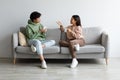 Young Asian boyfriend and girlfriend drinking coffee and chatting while sitting on sofa at home Royalty Free Stock Photo