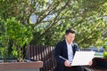 Young asian business man or freelancer sitting on bench and working with laptop in city park on modern urban street background Royalty Free Stock Photo