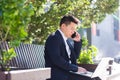 Young asian business man, freelancer sitting on bench, working with laptop in city park on modern urban street background outdoors Royalty Free Stock Photo