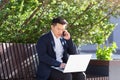 Young asian business man, freelancer sitting on bench, working with laptop in city park on modern urban street background outdoors Royalty Free Stock Photo