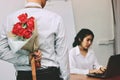 Young Asian business man holding a bouquet of red roses behind his back for girlfriend in valentines day. Love and romance in work Royalty Free Stock Photo