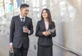Young Asian business man holding cup of coffee  walking  in public walkway with young business woman , smiling and talking Royalty Free Stock Photo