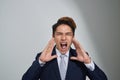 Young Asian business man shouting with hands cupped to his mouth, isolated on gray background Royalty Free Stock Photo