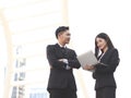 Young Asian business man and woman, standing outdoor with city building background. A man crossing his arms while woman using Royalty Free Stock Photo