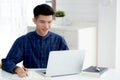 Young asian business man writing on notebook for planning working and using laptop computer on desk at home. Royalty Free Stock Photo