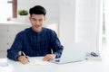Young asian business man writing on notebook for planning working and using laptop computer on desk at home. Royalty Free Stock Photo