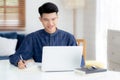 Young asian business man writing on notebook for planning working and using laptop computer on desk at home. Royalty Free Stock Photo