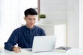 Young asian business man writing on notebook for planning working and using laptop computer on desk at home. Royalty Free Stock Photo