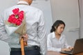 Young Asian business man holding a bouquet of red roses behind his back for girlfriend in valentines day. Love and romance in work Royalty Free Stock Photo