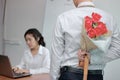 Young Asian business man holding a bouquet of red roses behind his back for girlfriend in valentines day. Love and romance in work Royalty Free Stock Photo