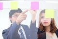 Young Asian business people use post it notes on glass wall to share idea at meeting room. Teamwork and brainstorm concept. Royalty Free Stock Photo