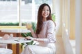 Young Asian business woman in casual clothes smile and sitting in cafe holding a glass of juice and looking out the window Royalty Free Stock Photo