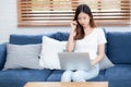 Young asian business woman smile and work from home with laptop computer online to internet on sofa in living room. Royalty Free Stock Photo