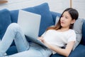 Young asian business woman smile and work from home with laptop computer online to internet on sofa in living room. Royalty Free Stock Photo
