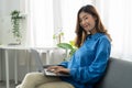 Young asian business woman smile and work from home with laptop computer online to internet on sofa in living room Royalty Free Stock Photo