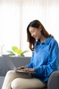 Young asian business woman smile and work from home with laptop computer online to internet on sofa in living room Royalty Free Stock Photo