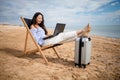 Asian business woman with tablet computer during tropical beach vacation. Freelancer working on laptop lying on sun lounger. Royalty Free Stock Photo