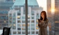 Young Asian business woman using cell phone standing at office window. Royalty Free Stock Photo