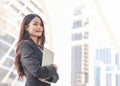 Young Asian business woman wearing black  suit, holding computer laptop, smiling and looking away. Outdoor with city  building Royalty Free Stock Photo