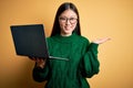 Young asian business woman wearing glasses and working using computer laptop smiling cheerful presenting and pointing with palm of Royalty Free Stock Photo