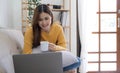 Young asian business woman work from home with laptop computer and drinking coffee on sofa in living room, freelance girl using Royalty Free Stock Photo