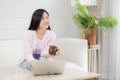 Young asian business woman work from home with laptop computer and drinking coffee on sofa in living room. Royalty Free Stock Photo