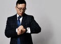 Young asian businessman expert in official jacket, tie and glasses stands looking at his watches checking time Royalty Free Stock Photo