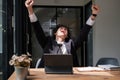 young asian businessman with hands stretched pose while working on laptop, celebrating Victory in office Royalty Free Stock Photo