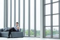 Young Asian businessman look at tablet sitting on sofa happy smile . The big window in the modern office. Royalty Free Stock Photo