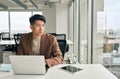 Young Asian businessman looking away thinking working on laptop in office. Royalty Free Stock Photo