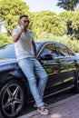 A young Asian businessman, a man in sunglasses, stands near a modern car and talks on a mobile phone, solves problems and Royalty Free Stock Photo