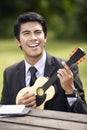 Young Asian businessman playing ukulele in a park. Conceptual image Royalty Free Stock Photo